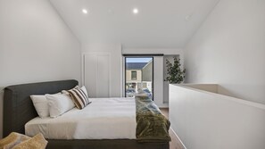 Een slaapkamer met een bed, kussens, een deken, een plant en uitzicht op buiten.