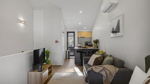 A modern living room with a TV, sofa, and a kitchen in the background.