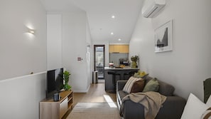 A modern living room with a TV, sofa, and a kitchen in the background.