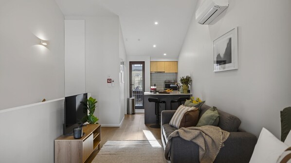 A modern living room with a TV, sofa, and a kitchen in the background.