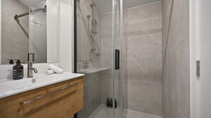 Een moderne badkamer met een glazen douchecabine, een houten wastafelmeubel en een grote spiegel.