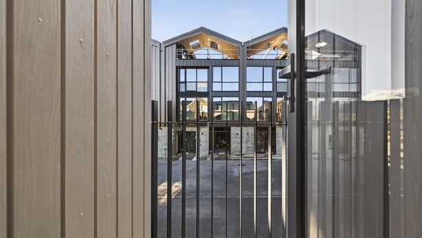 A gated entrance to a building with a modern architectural design, featuring large windows and a visible construction area.