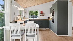 Een moderne keuken met een houten plafond, een eethoek met witte stoelen en een groot raam.