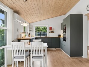 Eine moderne Küche mit Holzboden, einem Essbereich mit weißen Stühlen und einem großen Fenster.