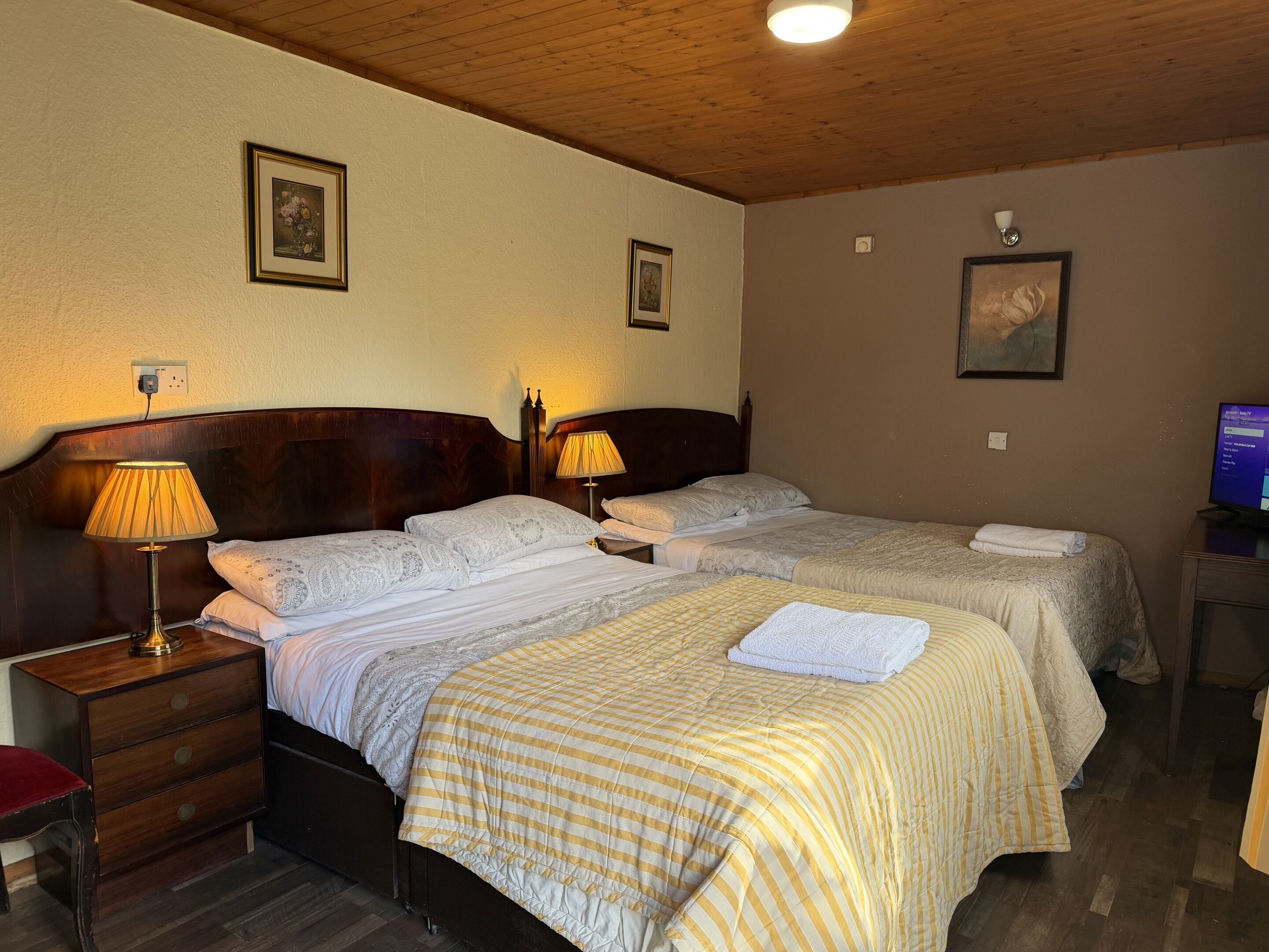 Ein Hotelzimmer mit zwei Betten, Holzkopfteilen, Nachttischlampen, einem Fernseher und einem kleinen Schreibtisch.