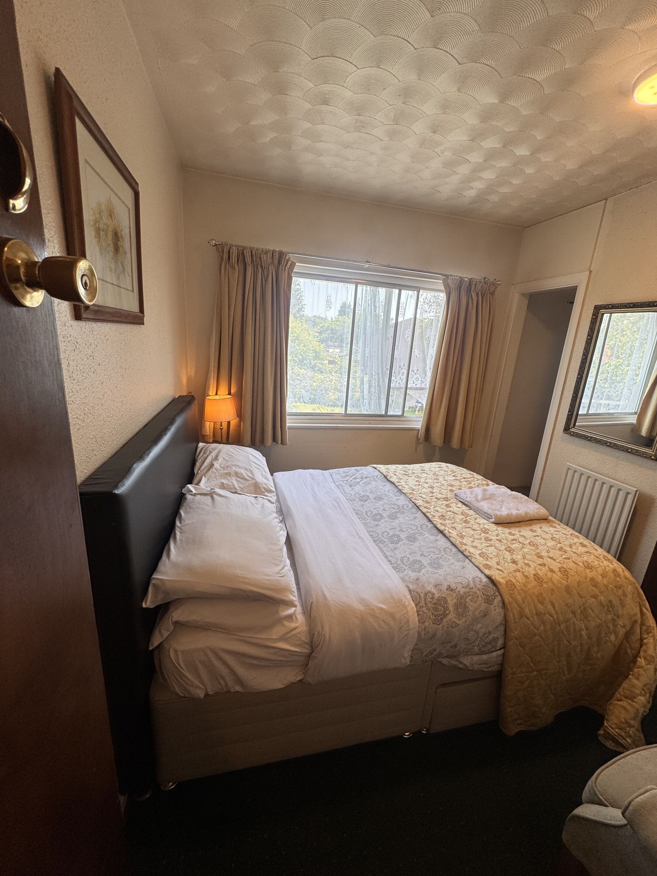 Un dormitorio con cama, ventana con cortinas, radiador y un cuadro en la pared.