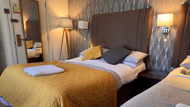 Habitación de hotel con dos camas, una lámpara de noche, un espejo y una pared con diseño.