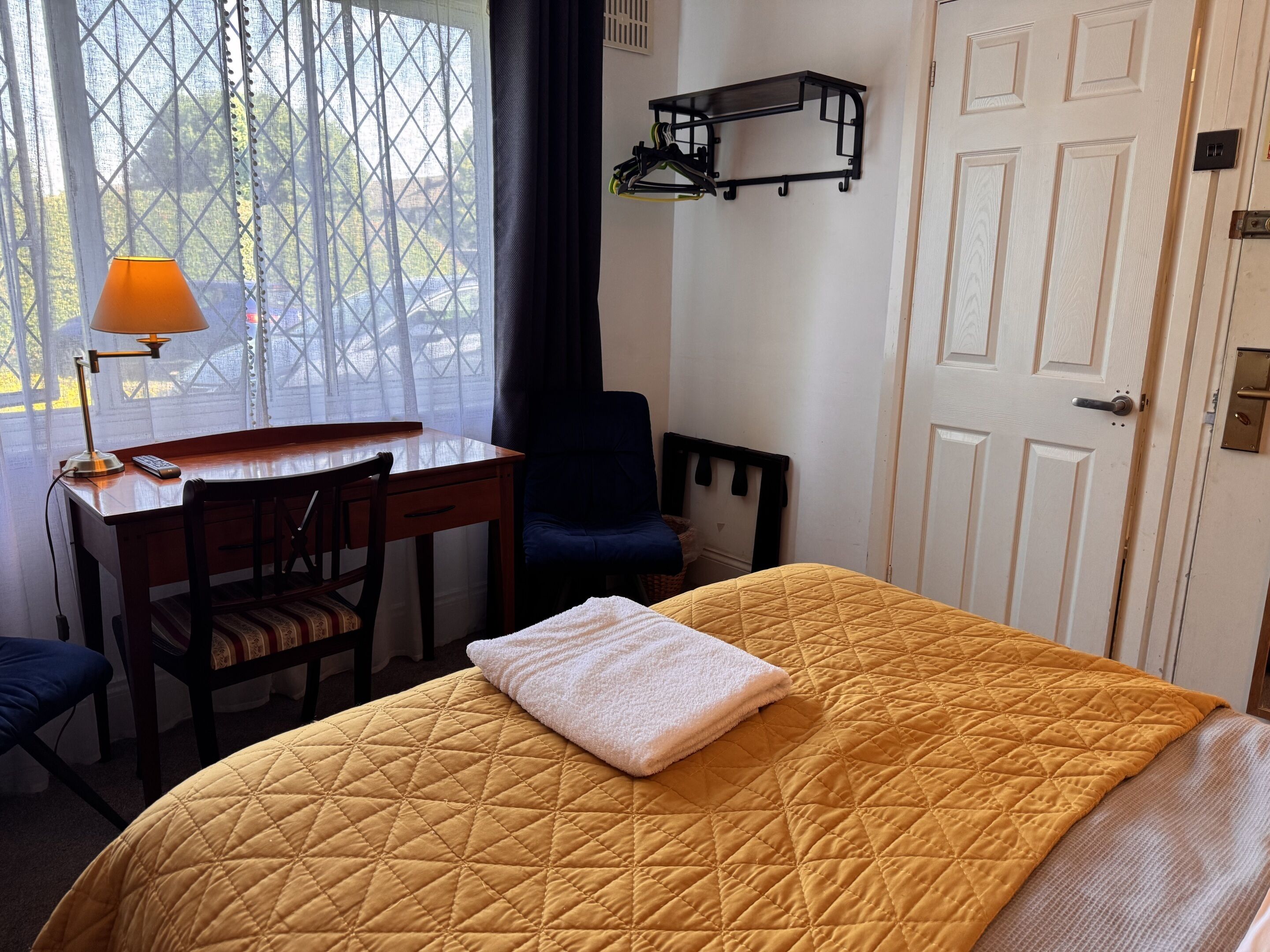 A hotel room with a bed, a desk, a chair, a hanging coat rack, and a door.