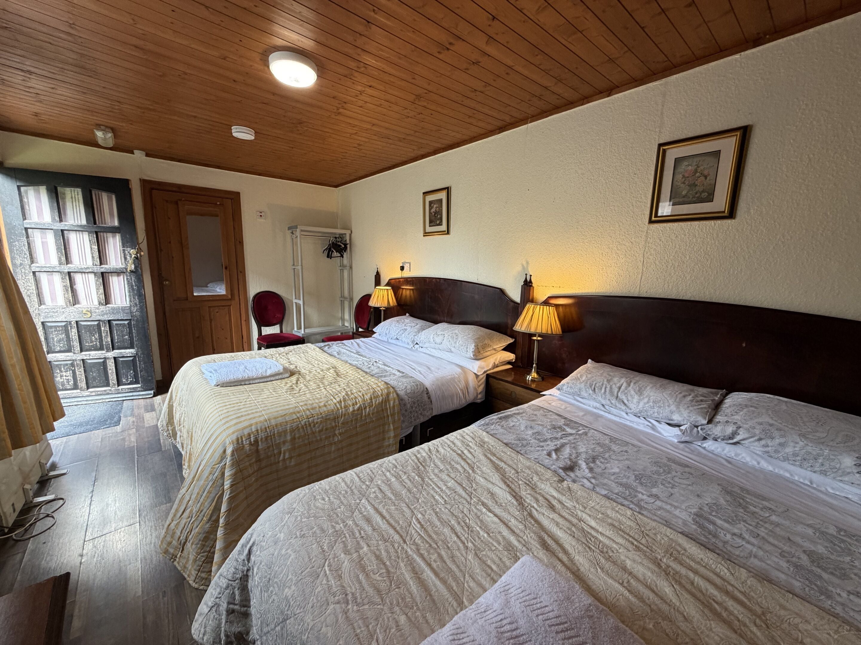 Habitación de hotel con dos camas, techo de madera, una puerta con cortinas, un cuadro en la pared y una lámpara en la mesita de noche.