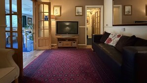 Una sala de estar con televisor, sofá, alfombra estampada y puerta corrediza que da a otra habitación.