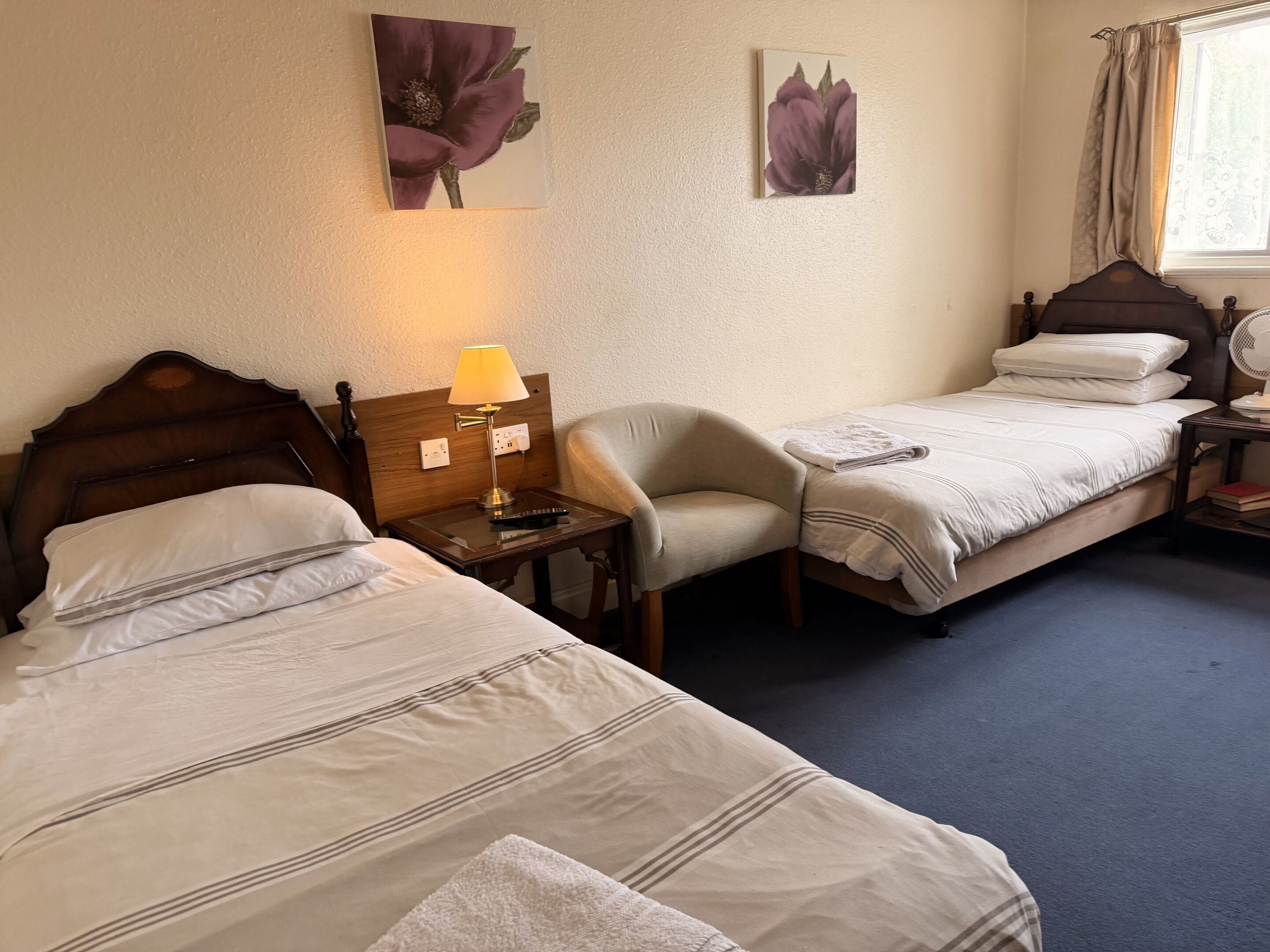 Habitación de hotel con dos camas, una silla, una mesita de noche con lámpara y una obra de arte en la pared.