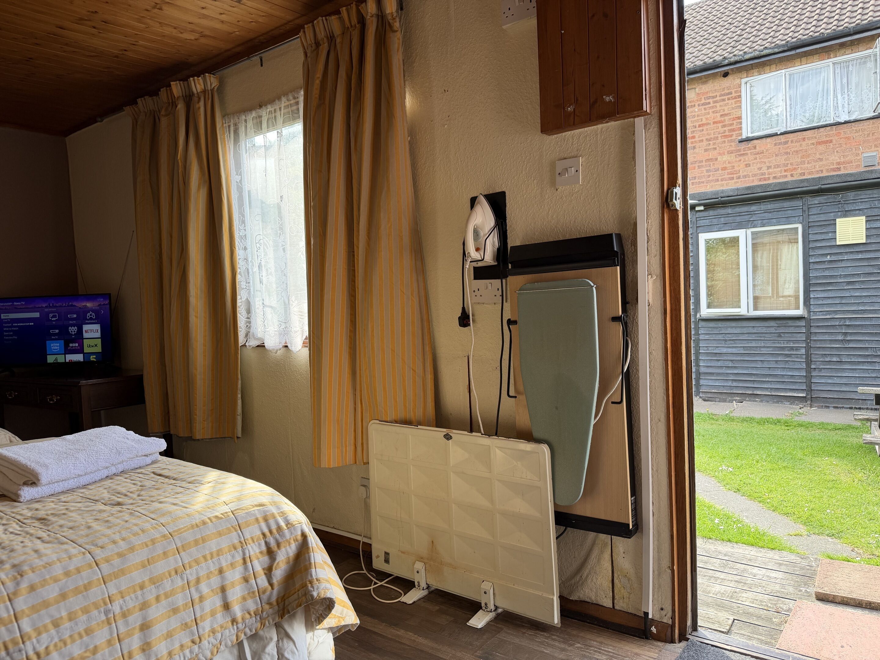 Ein Zimmer mit Bett, Vorhängen, Heizkörper, Fernseher und Blick nach draußen.