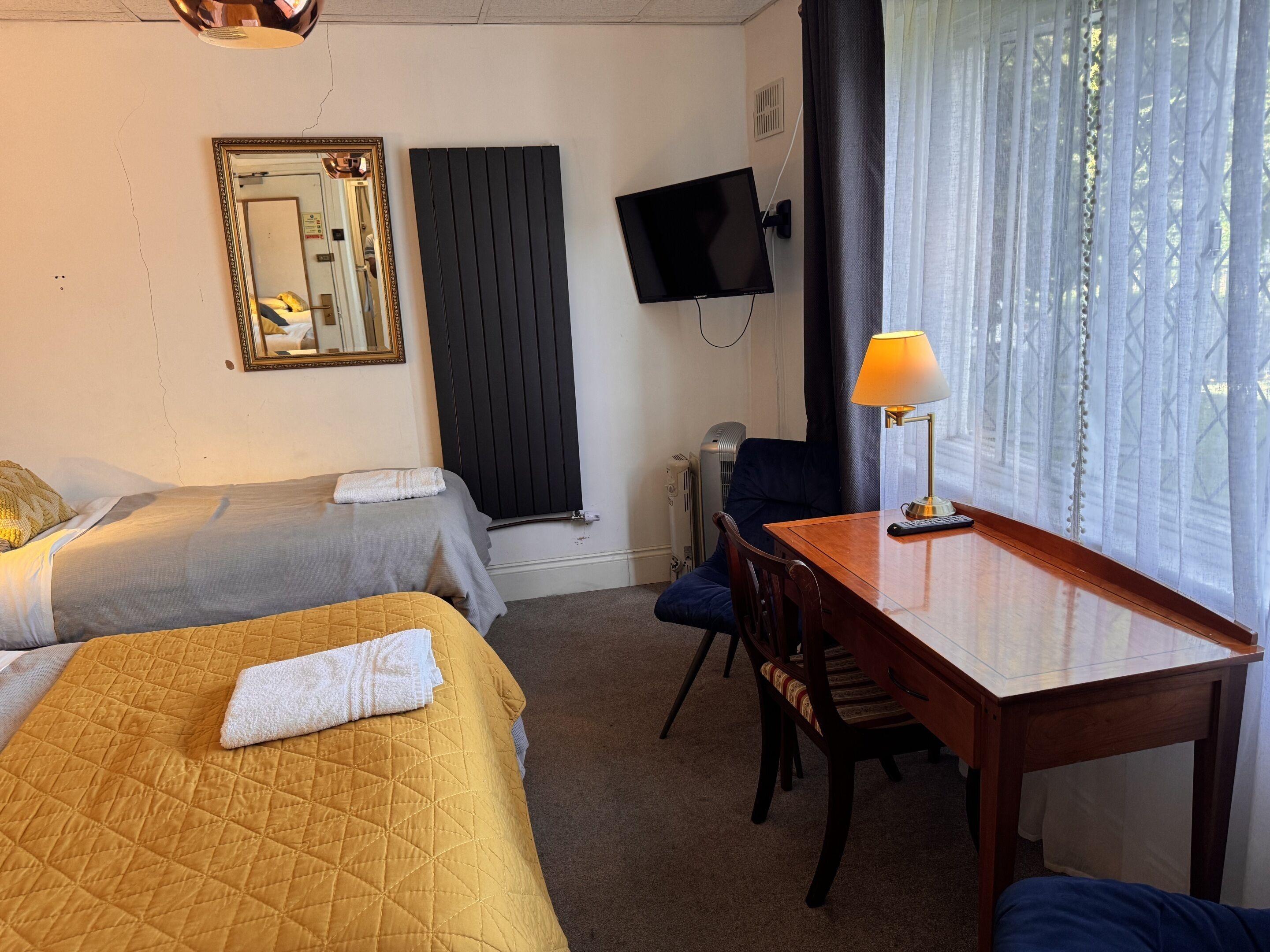 Une chambre d’hôtel avec deux lits, un bureau, une chaise, une télévision et une fenêtre avec des rideaux.