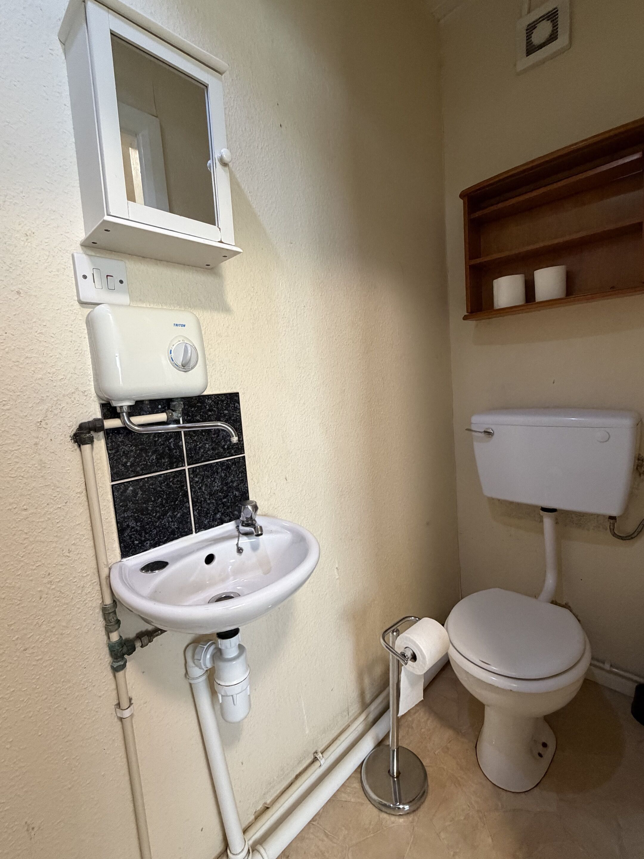 Un bagno con lavandino bianco, un water, uno specchio e uno scaffale con articoli da toilette.
