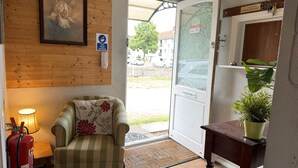 Un área de recepción con pared de madera, un cuadro enmarcado, un extintor, un sillón a rayas, una planta en maceta y un mostrador de recepción.