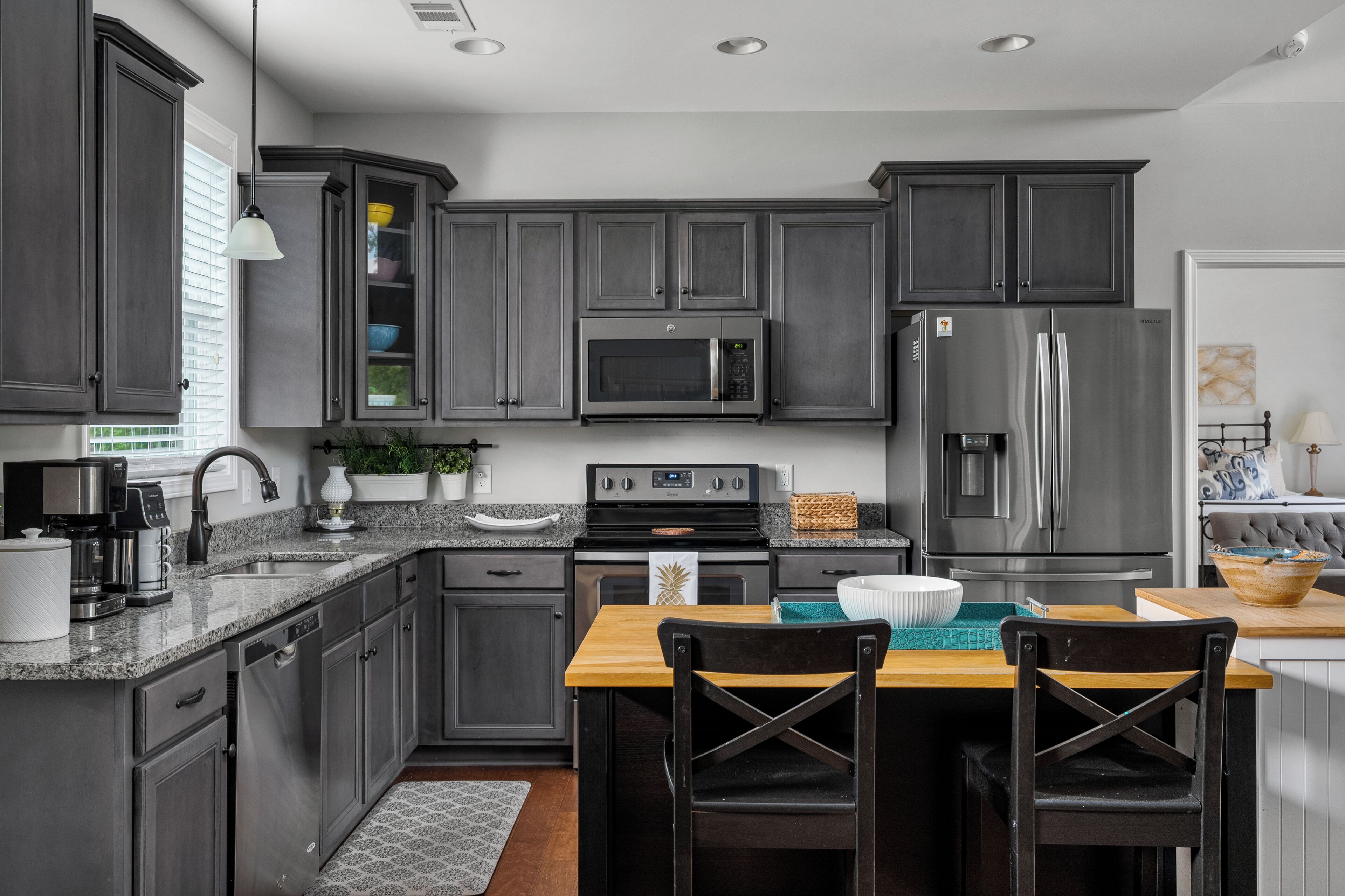 A modern kitchen with dark cabinets, stainless steel appliances, a wooden dining table, and black chairs.