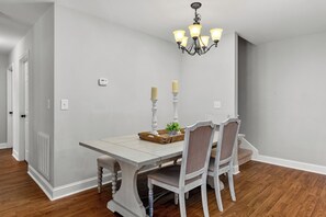Un coin repas avec une table blanche, quatre chaises, un lustre et une petite plante posée sur la table.