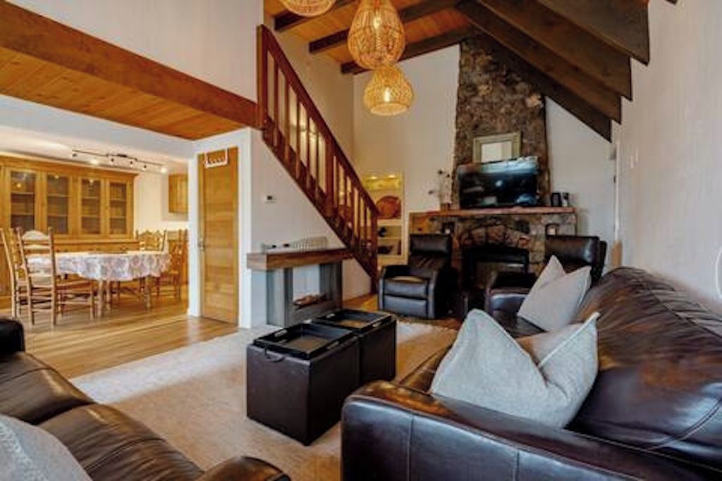 A spacious living area with a leather sofa, a dining table with chairs, and a staircase leading to an upper level.