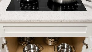 Una cucina con piano cottura a induzione, due pentole in acciaio inossidabile e una padella.