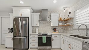 Una cocina moderna con armarios blancos, electrodomésticos de acero inoxidable, un horno empotrado y un lavamanos grande.