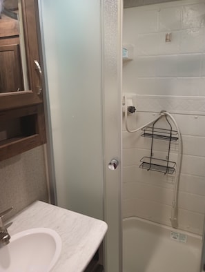 A bathroom with a white sink, a shower with a metal rack, and a wooden cabinet.