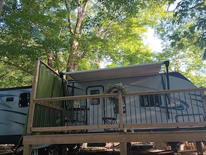 A recreational vehicle with a covered deck area, a small table, and a chair.