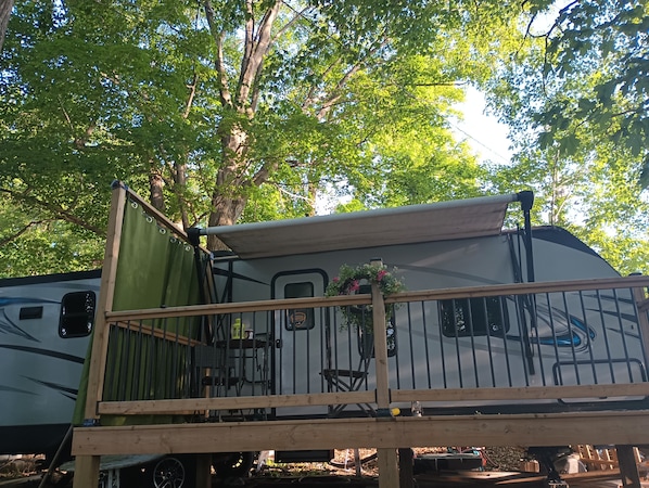 A recreational vehicle with a covered deck area, a small table, and a chair.