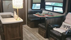A compact RV interior with a kitchenette, seating area, and two windows providing views. - Beautiful RV on Benson Lake (Westport)