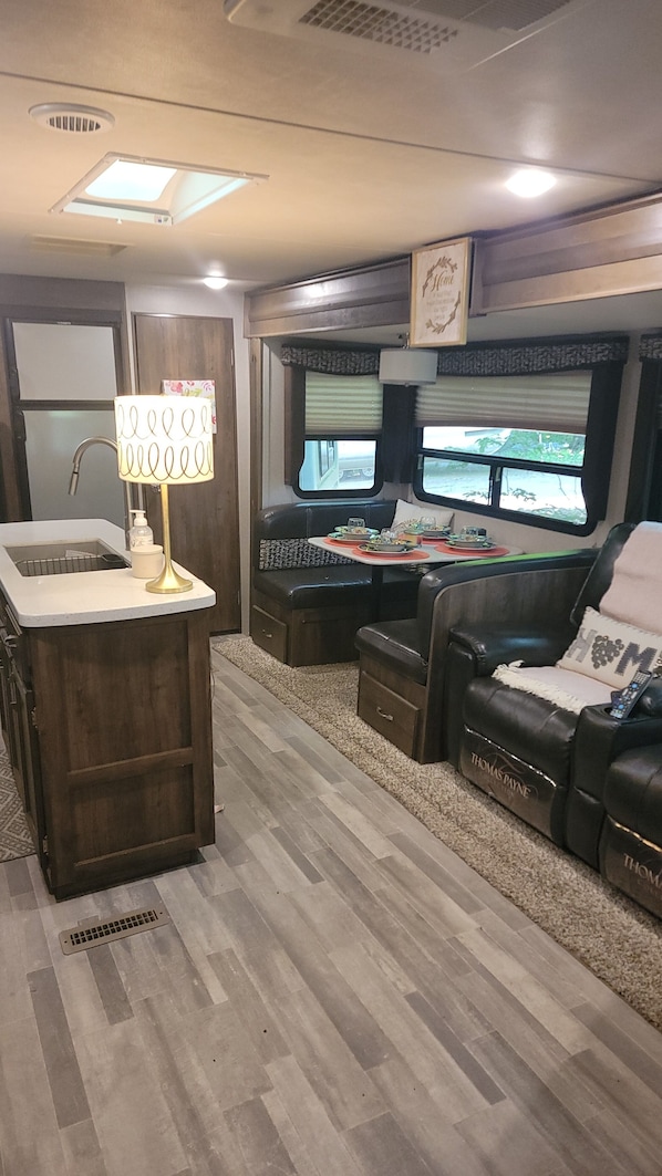 A compact RV interior with a kitchenette, seating area, and two windows providing views.