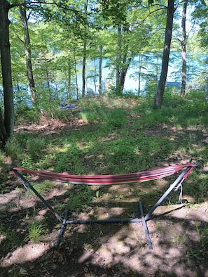 A hammock in a wooded area with a view of a body of water.