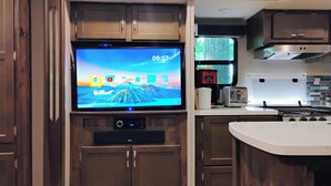 A kitchen with wooden cabinets, a built-in TV, a coffee maker, and a stove. - Beautiful RV on Benson Lake (Westport)