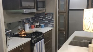 A kitchen with dark wooden cabinets, a stove, a microwave, and a refrigerator. - Beautiful RV on Benson Lake (Westport)