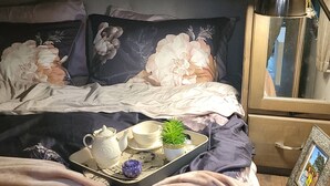 A bed with a floral duvet, a bedside table with a lamp, and a tray with a teapot and cups. - Beautiful RV on Benson Lake (Westport)