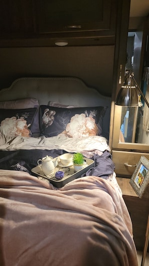 A bed with a floral duvet, a bedside table with a lamp, and a tray with a teapot and cups.