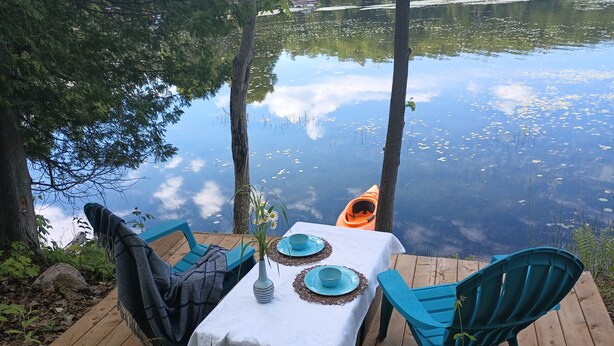 A wooden deck with a table set for two, overlooking a calm lake. - Beautiful RV on Benson Lake (Westport)