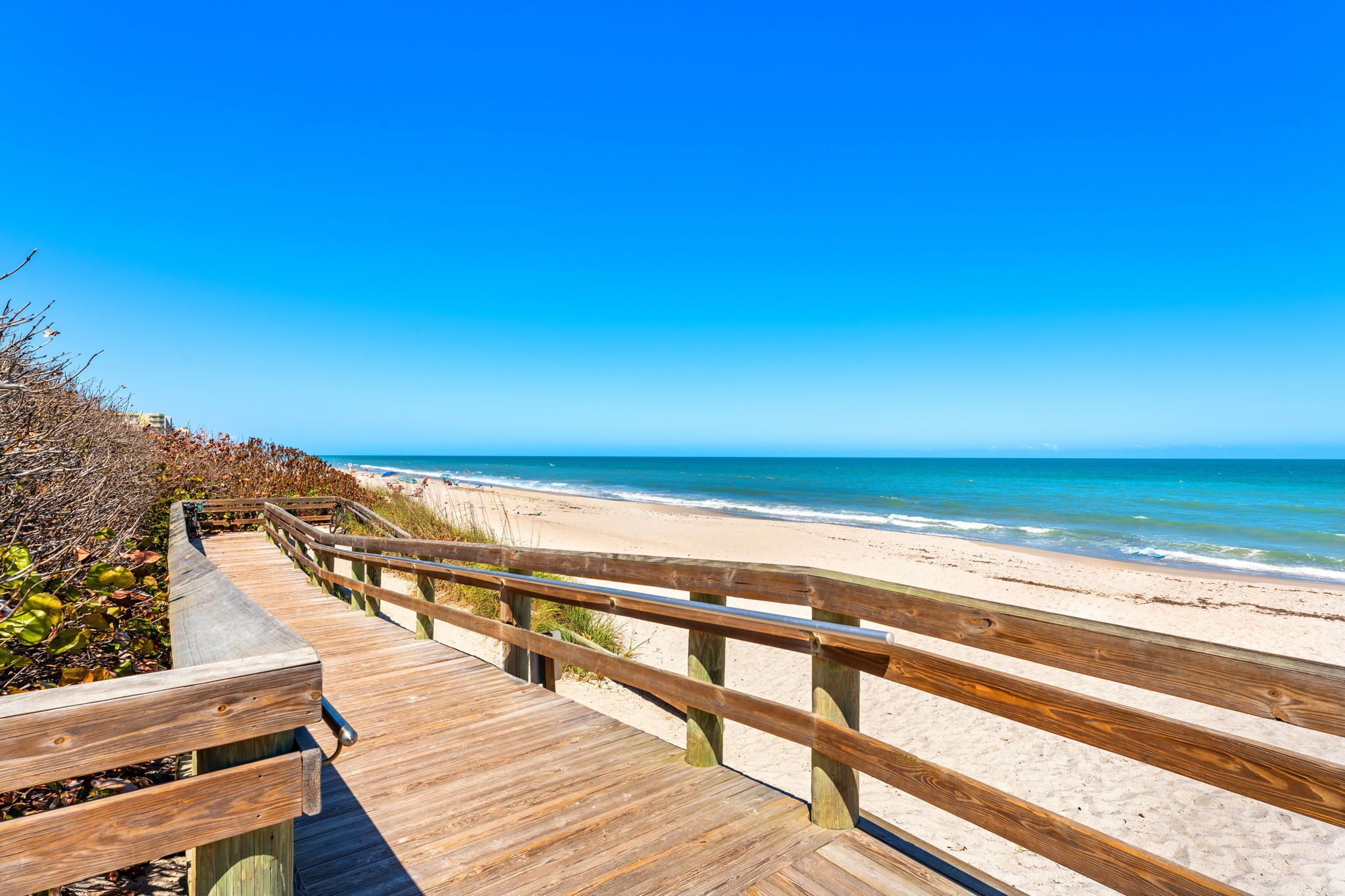 Une promenade en bois qui mène à une plage, avec un ciel bleu dégagé.