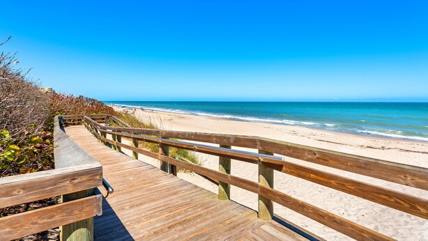 Une promenade en bois qui mène à une plage, avec un ciel bleu dégagé.
