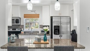 Une cuisine moderne avec des armoires blanches, des appareils en acier inoxydable, un comptoir en granit et des luminaires suspendus.
