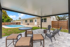 Een terras buiten met zwembad, zitgedeelte en uitzicht op een huis.