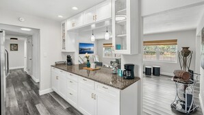 Une cuisine moderne avec des meubles blancs, des plans de travail en granit et des luminaires suspendus.