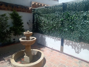 Un patio con una fuente de piedra, plantas en macetas y un muro de azulejos.