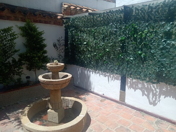 Een binnenplaats met een stenen fontein, potplanten en een betegelde muur.