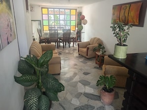 Una sala de estar con sofá, sillones, una mesa de comedor con sillas y plantas en macetas.