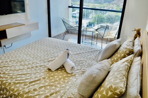 Ein Hotelzimmer mit einem großen Bett, einem an der Wand befestigten Flachbildfernseher, einem Balkon mit Stuhl und Blick auf die Stadt.