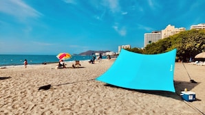 Une plage avec un parasol bleu, un autre parasol de plage et une glacière sur le sable.