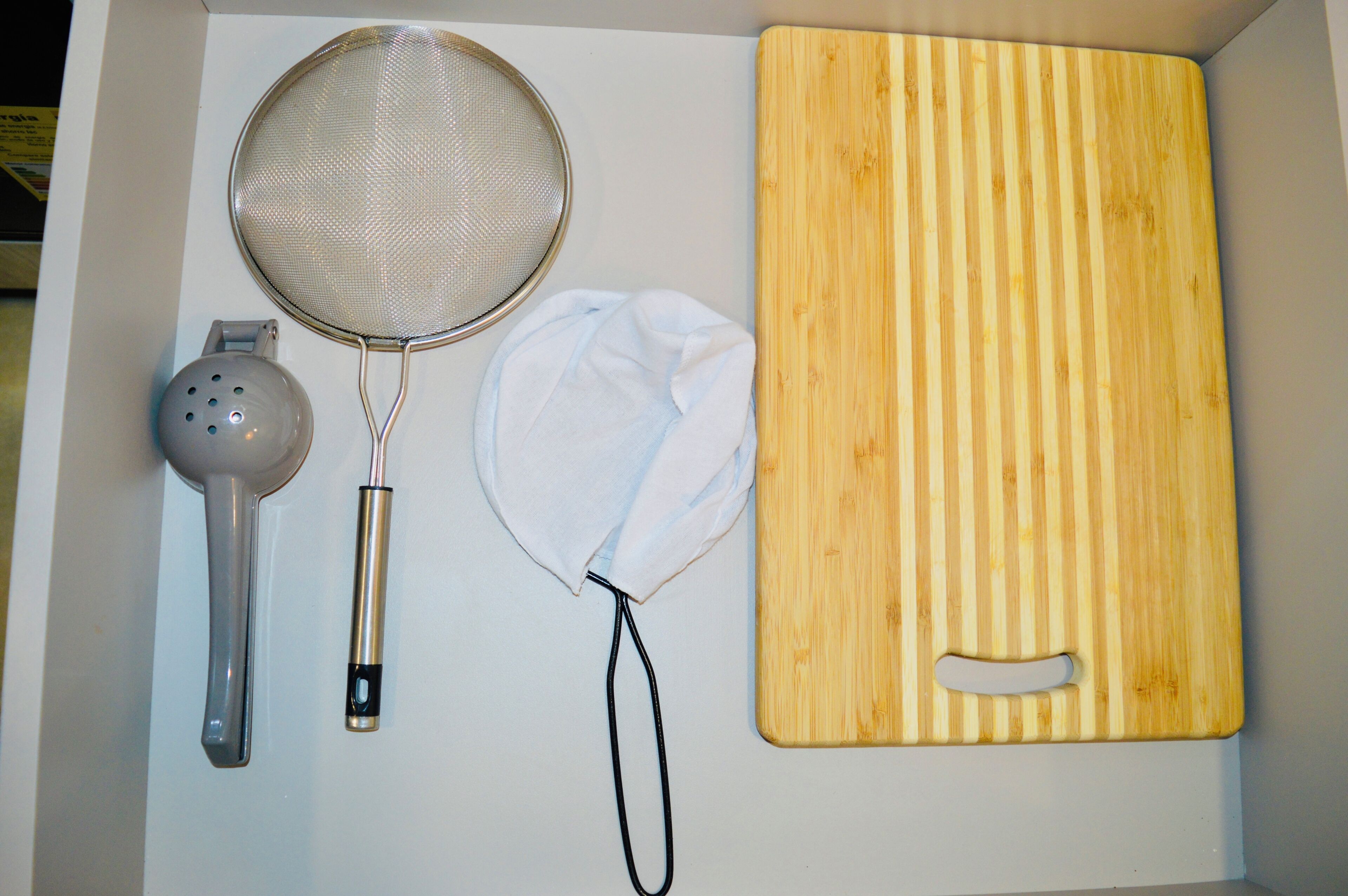 A kitchen with a wooden cutting board, a metal strainer, a colander, and a white cloth.