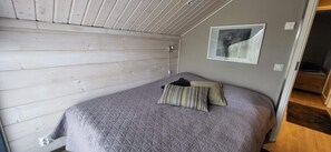 A bedroom with a wooden slat ceiling, a bed with a quilted mattress, two pillows, and a framed picture on the wall.