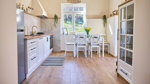 Cozinha com armários brancos, mesa de jantar com cadeiras, luminária pendente e janela com vista para o verde.