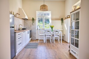 A kitchen with white cabinets, a dining table with chairs, a hanging light fixture, and a window with a view of greenery. - Adorable and premium 2-bedroom house with AC in welcoming Vrdnik (Vrdnik)