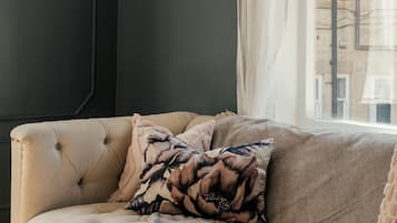 A room with a tufted sofa, a framed bird painting, and a window with a view of buildings.